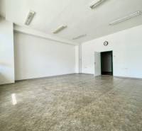 A spacious office with large windows, white walls, and ceiling lights.