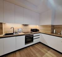 A kitchen unit in a 2-room apartment with white cabinets and a wooden countertop.