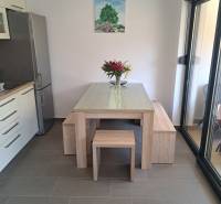 Dining area in a 3-room apartment with a wooden table, flowers, and a painting of a tree on the wall.