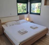 A bedroom in a three-room apartment with a double bed, windows, and a nightstand.