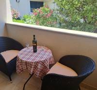 The balcony of a 3-room apartment with a pair of chairs and a table with wine and glasses.