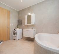 A bathroom in a family house with a bathtub, washing machine, and furniture in neutral tones.