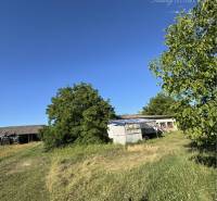 Residential plots in Povoda with grassy area and an older building in the background.