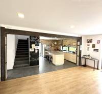 Interior of a family house with a staircase, wooden floor, and kitchen in the background.