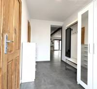A narrow interior of a family house with wooden doors and white cabinets.