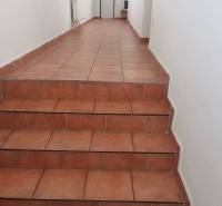 A corridor in a building with white walls and terracotta flooring, leading to white doors.