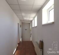 A corridor in a building with white walls, windows, and ceramic flooring.
