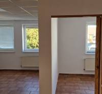 Interior of a building with white walls, brown tiles, and three windows with a view.