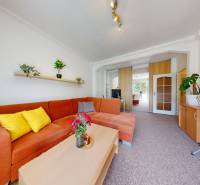 Living room with an orange couch, flowers on the table, shelves with plants in a 2-room apartment.