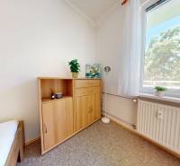 A room of a two-room apartment with a window, a wardrobe, a bed, and a light floor.