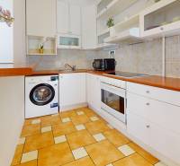 A kitchen in a 2-room apartment with white cabinets, appliances, and tiles.