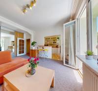 A living room in a two-room apartment with an orange sofa and a table, illuminated by interior doors.