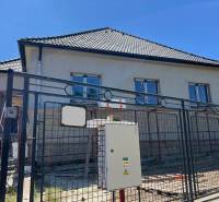 A family house in Sasinkovo on Sasinkovo Street with an unfinished facade behind a metal fence.