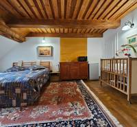 A bedroom in a family house with a wooden ceiling, a bed, a baby crib, and a carpet.