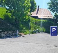 Parking lot on Donovaly Street in the town of Donovaly near family houses, with trees and grass.