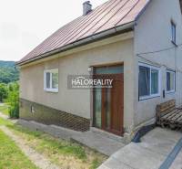 A family house in Dolná Mariková with a grassy yard and a paved access road, surrounded by nature.