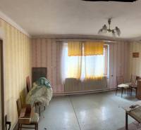 A room in a family house with older furnishings and yellow curtains on the windows.