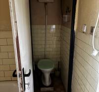 A small tiled toilet in a family house, showing an older flushing system.