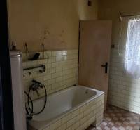 A bathroom in a family house with a bathtub, tiles, a boiler, and a window with a lace curtain.