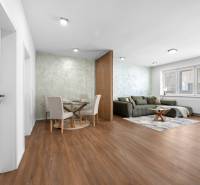 Living room in a three-room apartment with wooden flooring, a sofa, and a dining table.