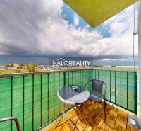 A balcony in a studio apartment with a view of Senec, seating, and a cloudy sky.