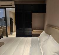 A bedroom with a white bed and a black wardrobe, next to the kitchen unit.