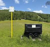 A meadow in Nová Bystrica with a mining cart and a signpost next to a cottage.