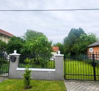 A family house in Dunaszeg with a gate, front garden, and trees.