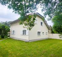A family house in Dunaszige with a white facade, a landscaped garden, and trees.