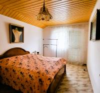 A bedroom in a family house with a wooden ceiling, a painting, and a decorative chandelier.