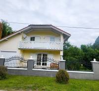 Yellow family house in Dunaszige, with a balcony and a garden, enclosed by a black fence.