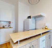 A kitchen in a studio apartment with cabinets, a hood, and a wooden countertop.
