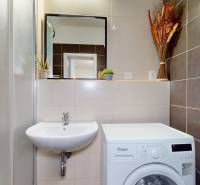 Bathroom with a washing machine, sink, and mirror in a studio apartment.