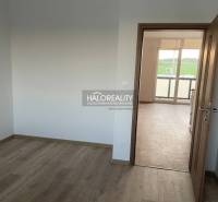 A room with white walls and doors leading to a bright room in a two-room apartment.