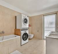 A bathroom in a family house with a bathtub, washing machine, dryer, and double sink.