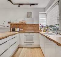 A kitchen in a family house with light cabinets, a wooden countertop, and large windows.