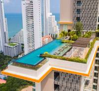 Apartment construction in Pattaya with a rooftop pool, with the sea and high-rise buildings in the background.