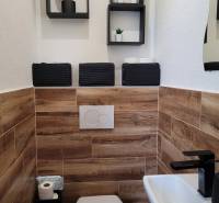 A toilet in a 3-room apartment with wooden paneling and black accessories.