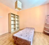 A room in a 3-room apartment with a bed, shelves, and wooden stairs.