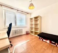 A room with a table, a chair, a shelf, and a bed in a three-room apartment.