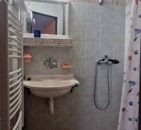 A bathroom in a cottage with ceramic tiles, a shower corner, and a sink.