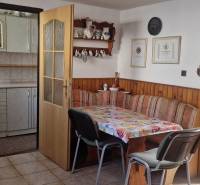 Dining room in a cottage with rustic furniture, flowers on the table, open doors to the kitchen.
