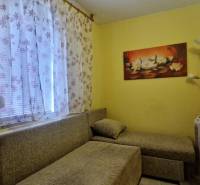 A room in a cottage with an armchair, floral curtains, and a painting of lotus flowers.