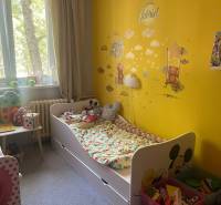 Children's room in a three-room apartment with a bed, toys, and a yellow wall with decorations.