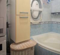 A bathroom in a 3-room apartment with a washing machine, a sink, a storage basket, and blue tiles.