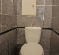 A bathroom with a toilet in a three-room apartment, tiled with gray marble tiles.