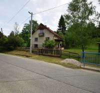 A family house in Veľká Lesná by the road, surrounded by greenery and a fence.