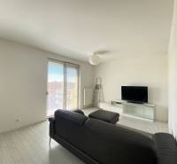 Living room in a 3-room apartment with white walls, TV, and a black sofa.