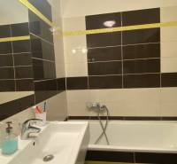 A bathroom in a three-room apartment with a bathtub and a sink, tiled with dark and light tiles.