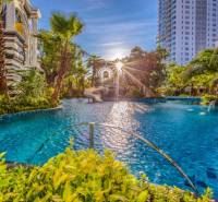 Apartment construction in Pattaya with a pool surrounded by greenery and palm trees in a sunny environment.
